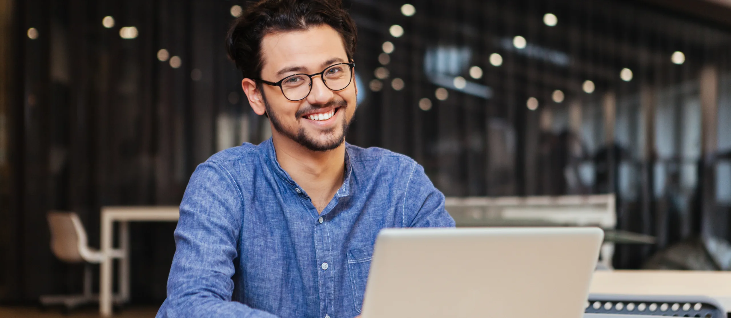 Lächelnder Mann mit Brille am Laptop in einem Büro